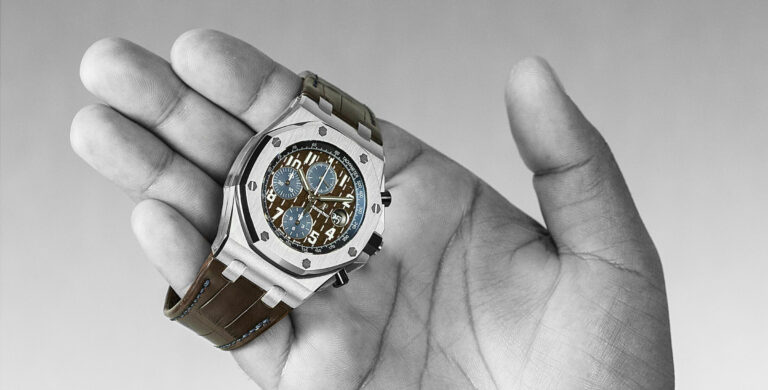 AUDEMARS PIGUET ROYAL OAK OFFSHORE SELFWINDING CHRONOGRAPH numa mão aberta. Foto a preto e branco, apenas com o relógio colorido com mostrador castanho e azul.