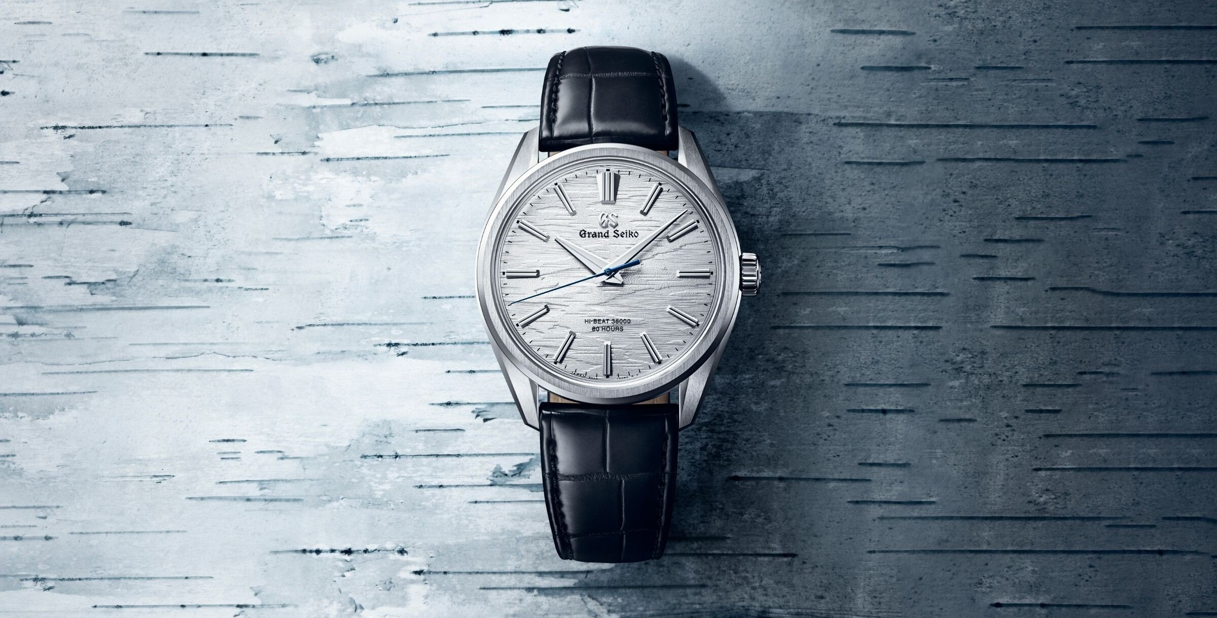 Relógio Grand Seiko SLGW003 visto de frente com mostrador branco texturado, caixa prateada e correia preta em pele de aligátor.