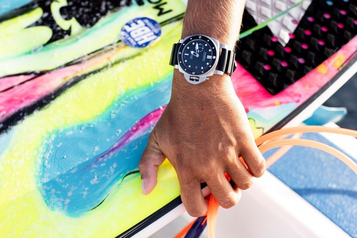 Imagem de uma mão em primeiro plano a segurar uma prancha de surf com um relógio Panerai Luminor no pulso
