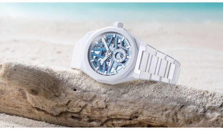 Relógio Zenith DEFY Skyline Skeleton White Ceramic pousado sobre um tronco de madeira na areia, com o mar desfocado ao fundo.