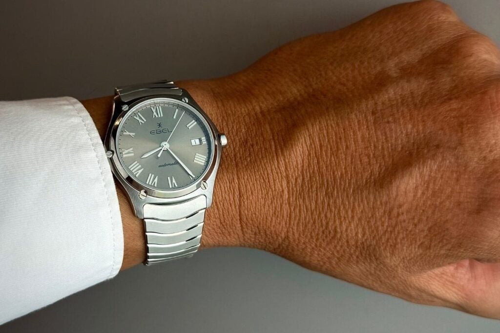 Pulso com relógio Ebel Classic com mostrador cinzento, numerais romanos e bracelete metálica em destaque