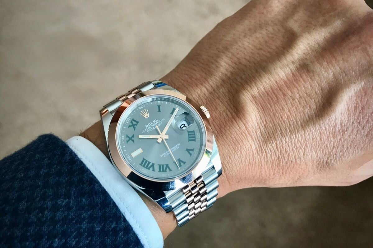 Relógio Rolex Datejust com mostrador cinza e numerais romanos verdes no pulso de uma pessoa.