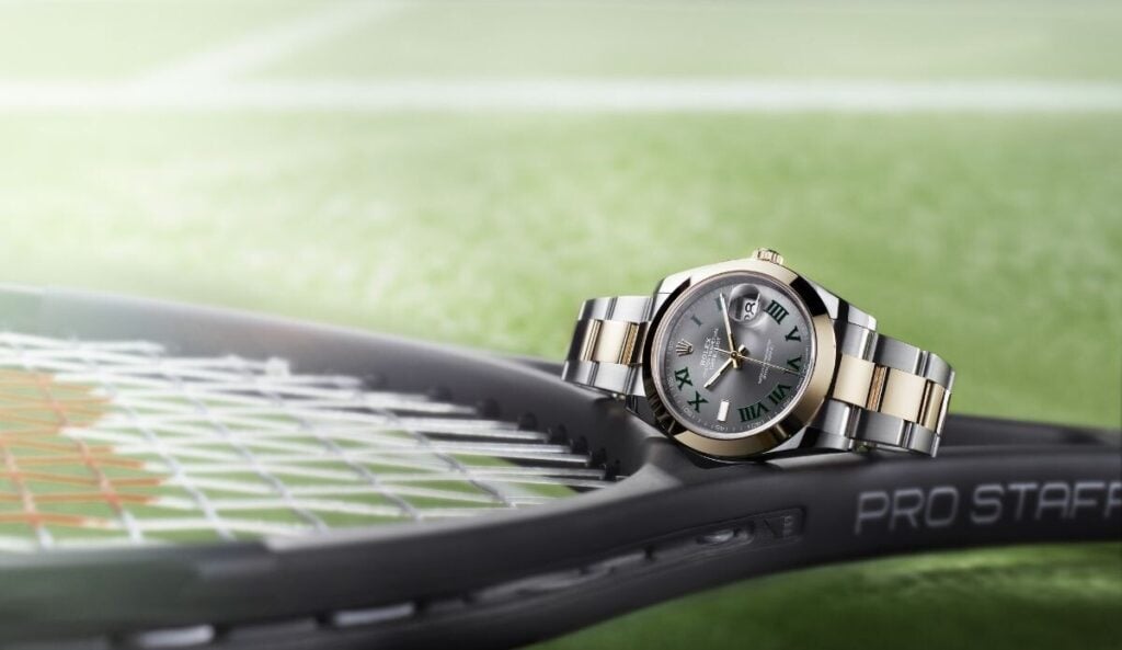 Relógio Rolex Datejust com mostrador wimbledon cinzento fotografado em primeiro plano, em cima de uma raquete de ténis