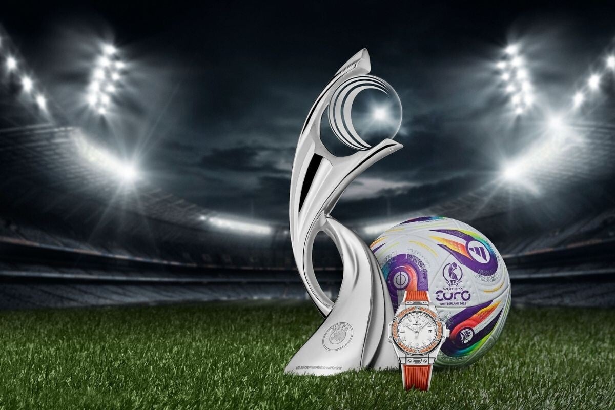 Troféu da Eurocopa Feminina 2025 ao lado da bola oficial e de um relógio Hublot em um estádio iluminado