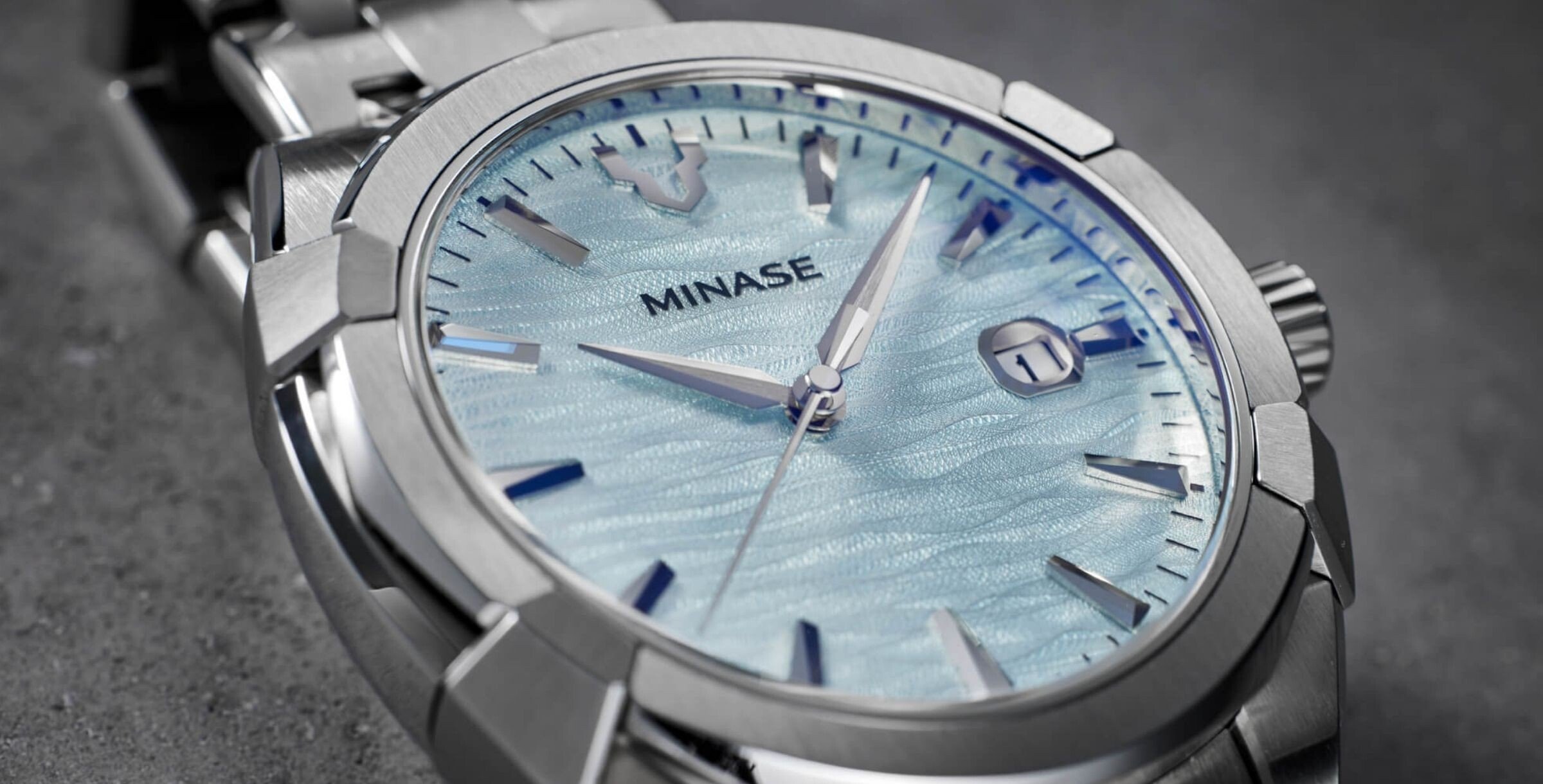 Close-up do mostrador do relógio Minase Uruga Ice Blue com textura ondulada azul claro e marcadores prateados.
