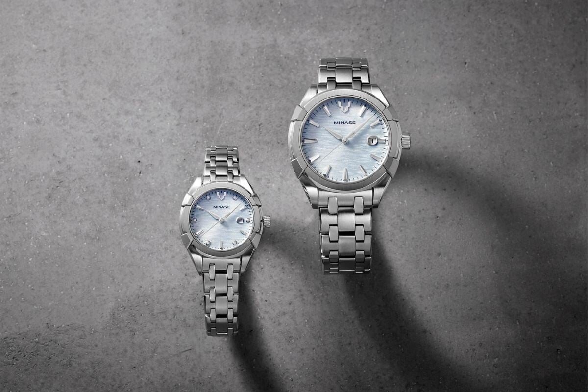Dois relógios Minase Uruga Ice Blue, um modelo masculino e outro feminino, exibidos sobre uma superfície metálica industrial.