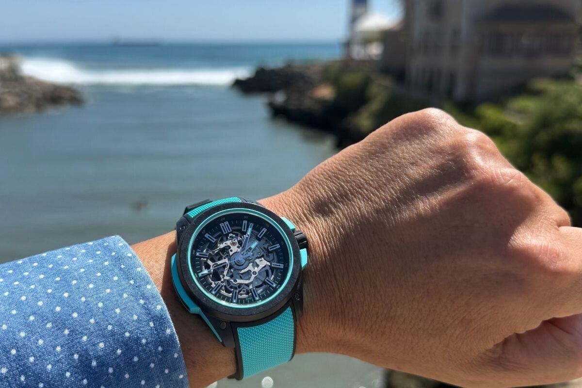 O relógio Norqain Wild Skeleton em tons de azul claro num pulso tendo Cascais como pano de funodo