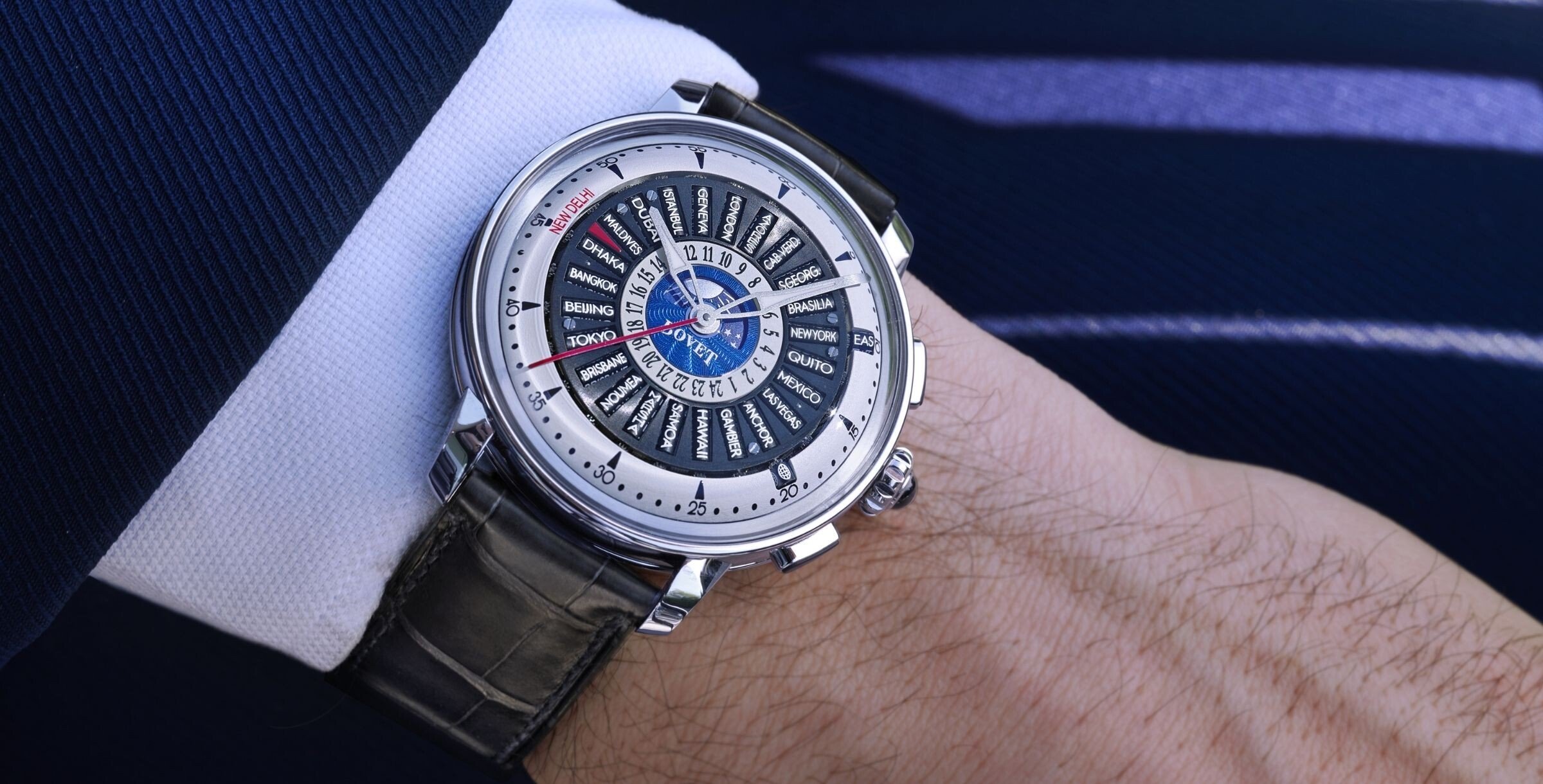 Relógio Bovet Récital 30 Worldtimer no pulso de um homem com casaco azul, destacando o mostrador com múltiplos fusos horários.