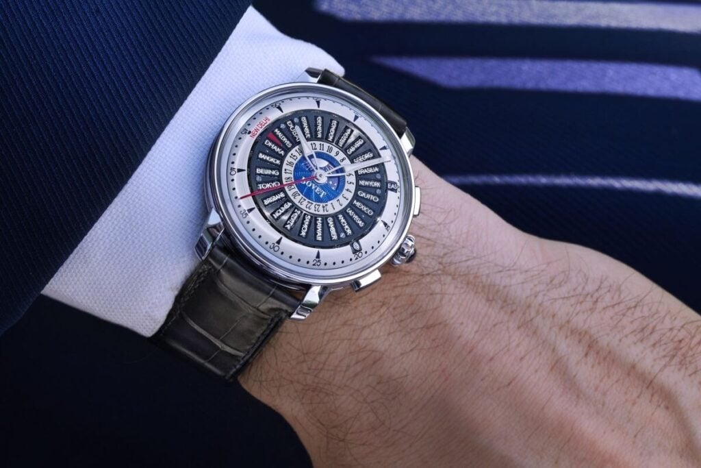 Relógio Bovet Récital 30 Worldtimer no pulso de um homem com casaco azul, destacando o mostrador com múltiplos fusos horários.