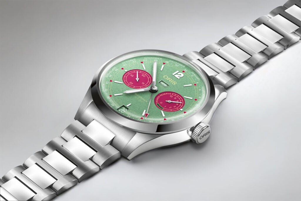 Relógio Oris Big Crown Calibre 113 - deitado sob fundo cinzento, com mostrador verde e submostradores cor de rosa.