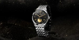 Relógio Tudor 1926 Moonphase em aço com mostrador preto e detalhes dourados, fotografado sobre fundo escuro estrelado.