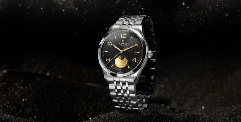 Relógio Tudor 1926 Moonphase em aço com mostrador preto e detalhes dourados, fotografado sobre fundo escuro estrelado.