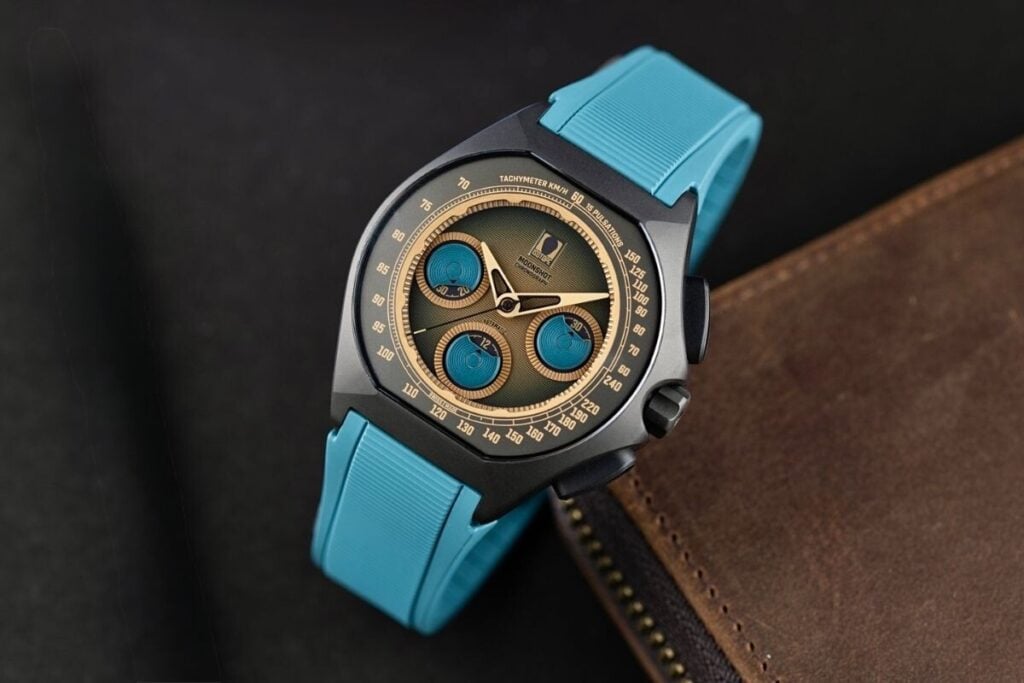 relógio em titânio preto com mostrador castanho e azul e bracelete azul em cima de uma mesa Isotope Chronograph Moonshot Terra Maris