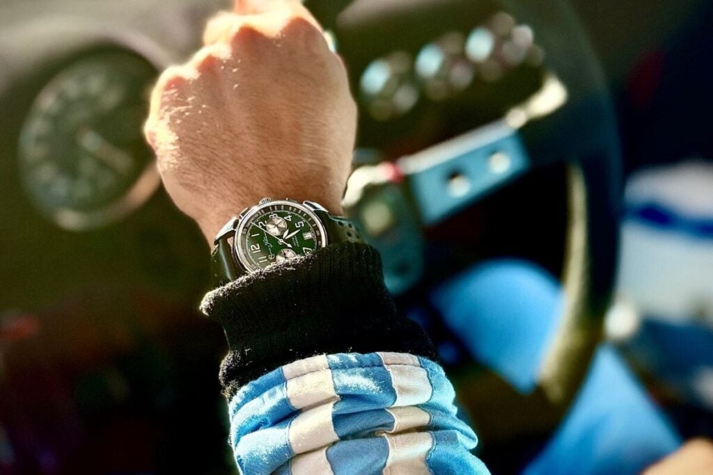 Relógio Cuervo y Sobrinos com mostrador verde no pulso de um piloto com fato às riscas, junto a um volante