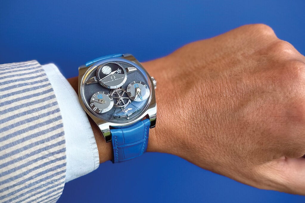 Relógio de pulso sofisticado com mostrador metálico azul e pulseira de couro azul, usado no pulso de uma pessoa vestindo camisa listrada.