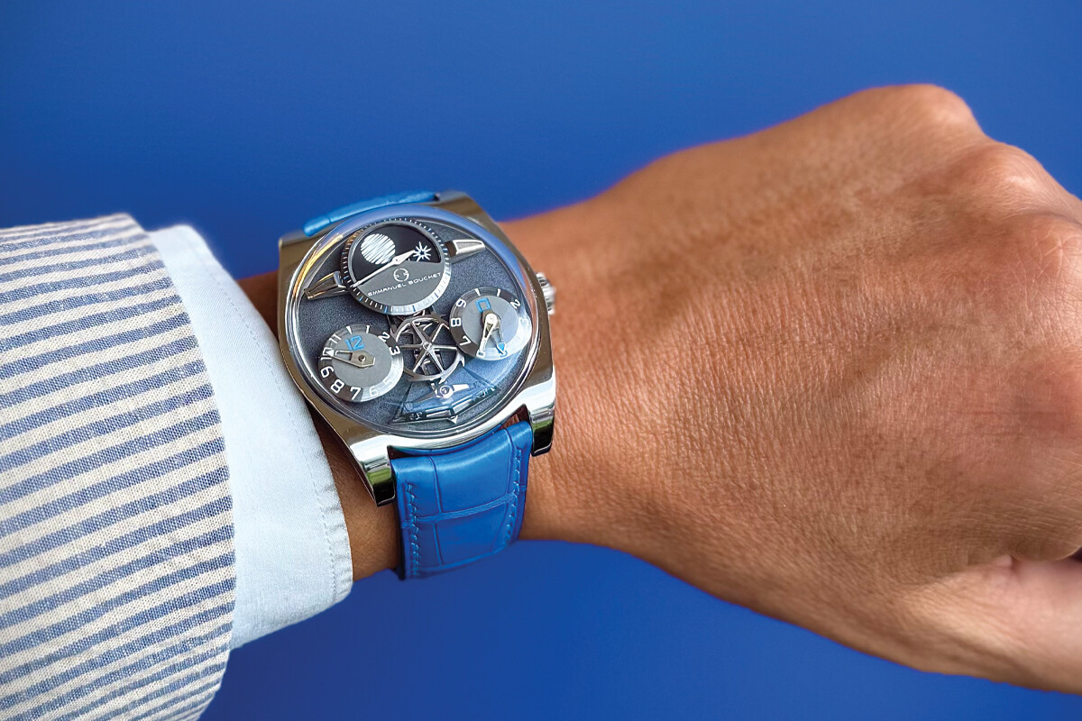 Relógio de pulso sofisticado com mostrador metálico azul e pulseira de couro azul, usado no pulso de uma pessoa vestindo camisa listrada.