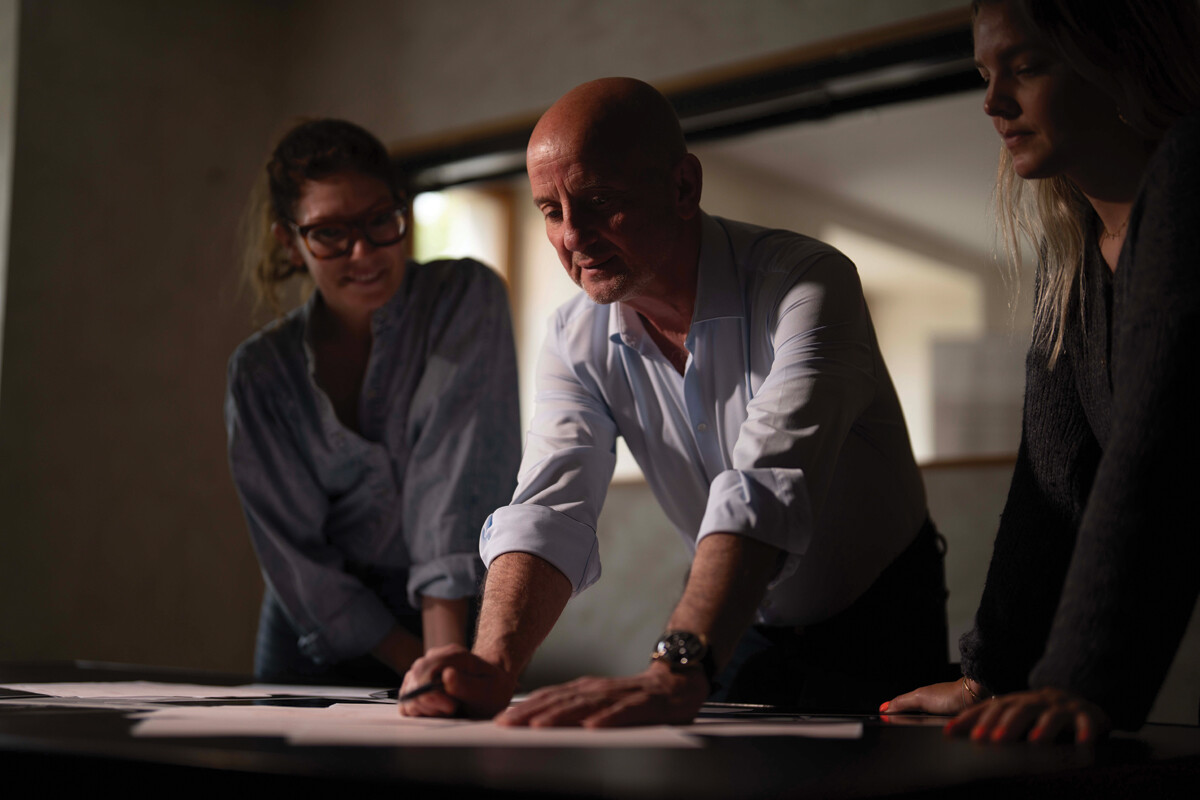 Três pessoas em uma reunião analisando documentos sobre uma mesa em ambiente iluminado suavemente.
