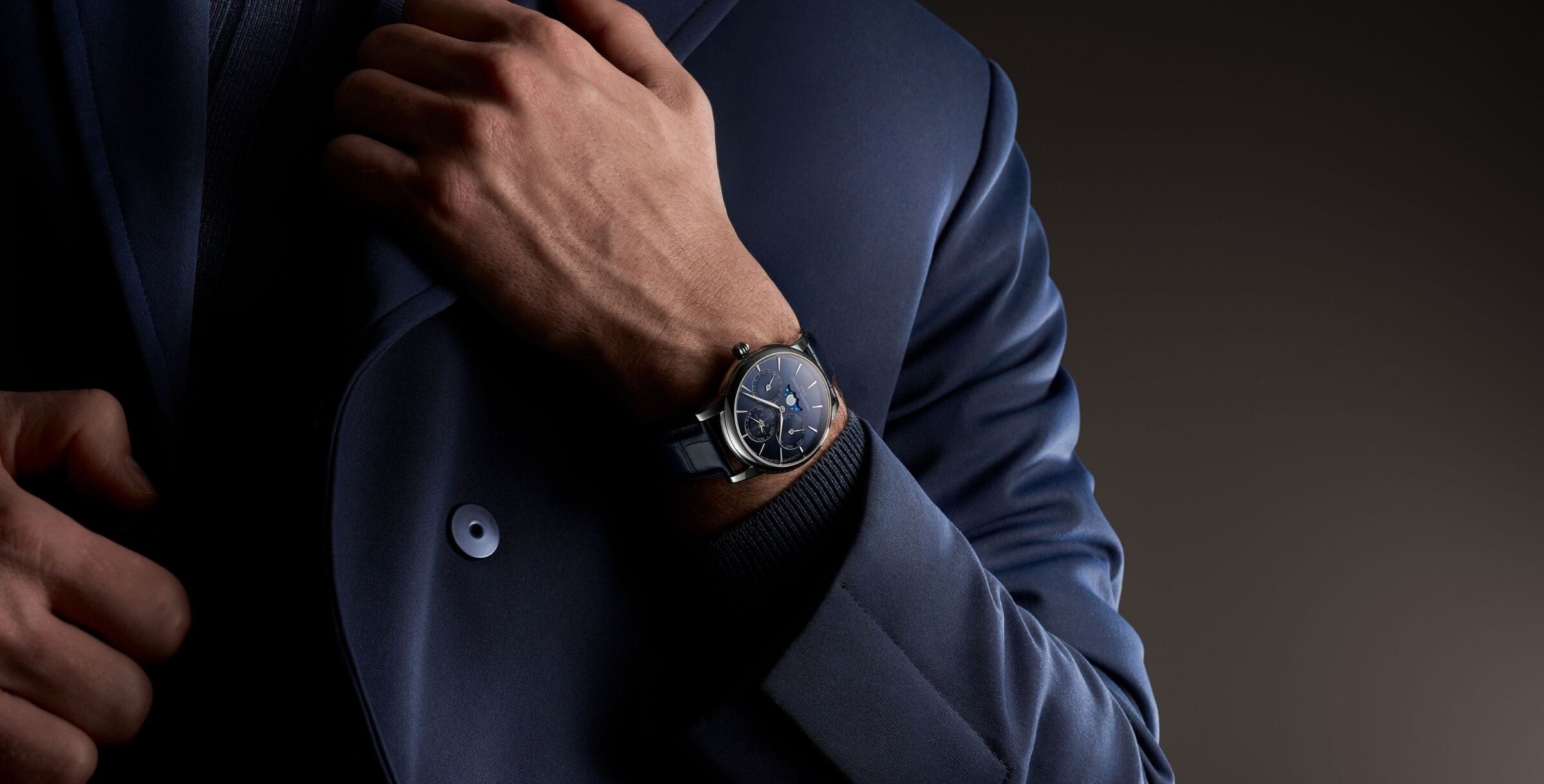 Frederique Constant Classic Perpetual Calendar Manufacture de mostrador azul escuro visto no pulso de um homem vestido com fato azul, num plano aproximado