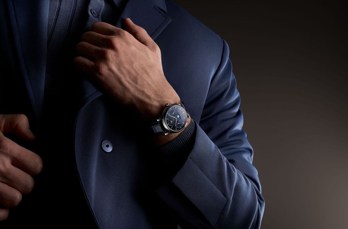 Frederique Constant Classic Perpetual Calendar Manufacture de mostrador azul escuro visto no pulso de um homem vestido com fato azul, num plano aproximado