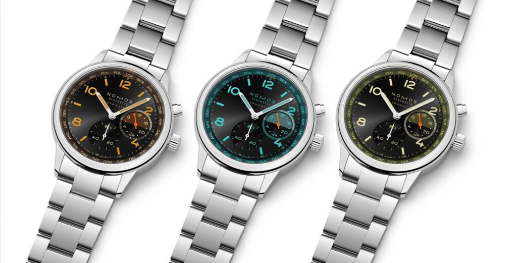 Três relógios de pulso NOMOS Glashütte com bracelete em aço inoxidável, mostradores pretos e detalhes coloridos em laranja, azul-turquesa e amarelo.