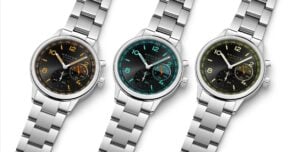 Três relógios de pulso NOMOS Glashütte com bracelete em aço inoxidável, mostradores pretos e detalhes coloridos em laranja, azul-turquesa e amarelo.