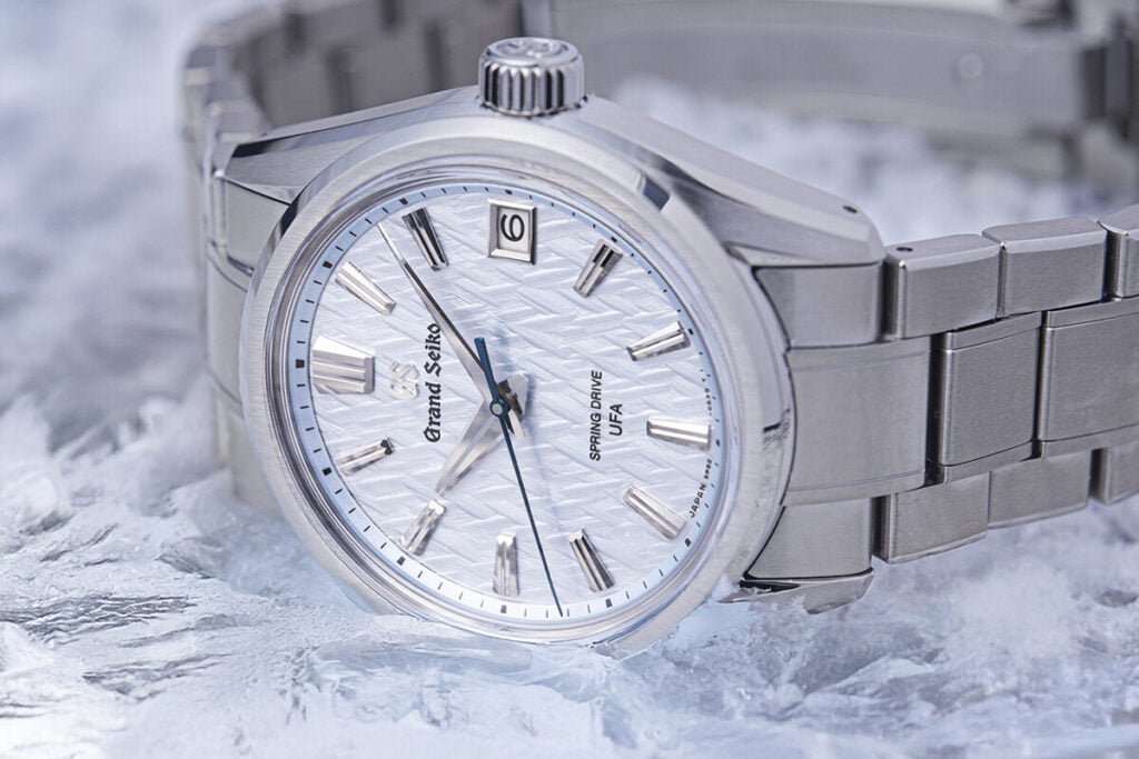 Relógio de pulso prateado com mostrador texturizado em tom claro e ponteiro dos segundos azul.