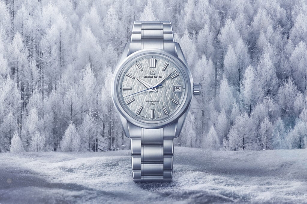 Relógio de pulso prateado com mostrador texturizado em tom claro e ponteiro dos segundos azul.