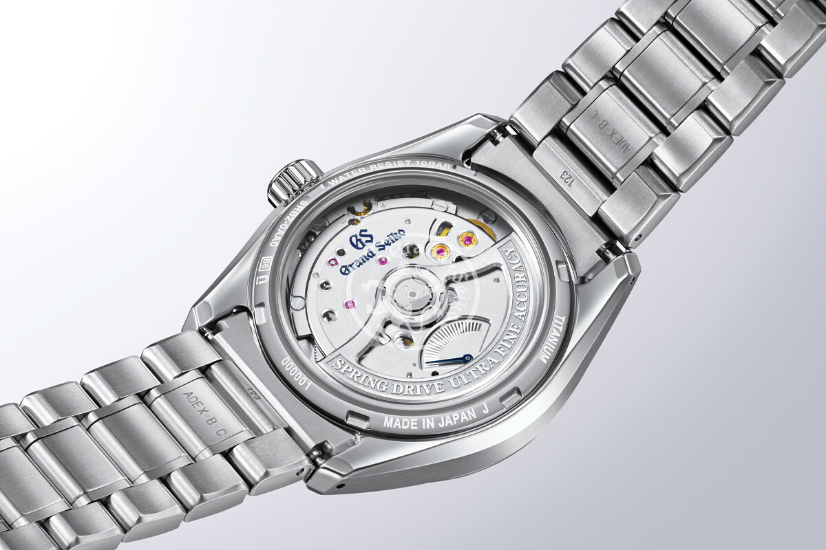 Vista traseira de um relógio de pulso metálico, mostrando o movimento mecânico visível através do fundo em vidro.