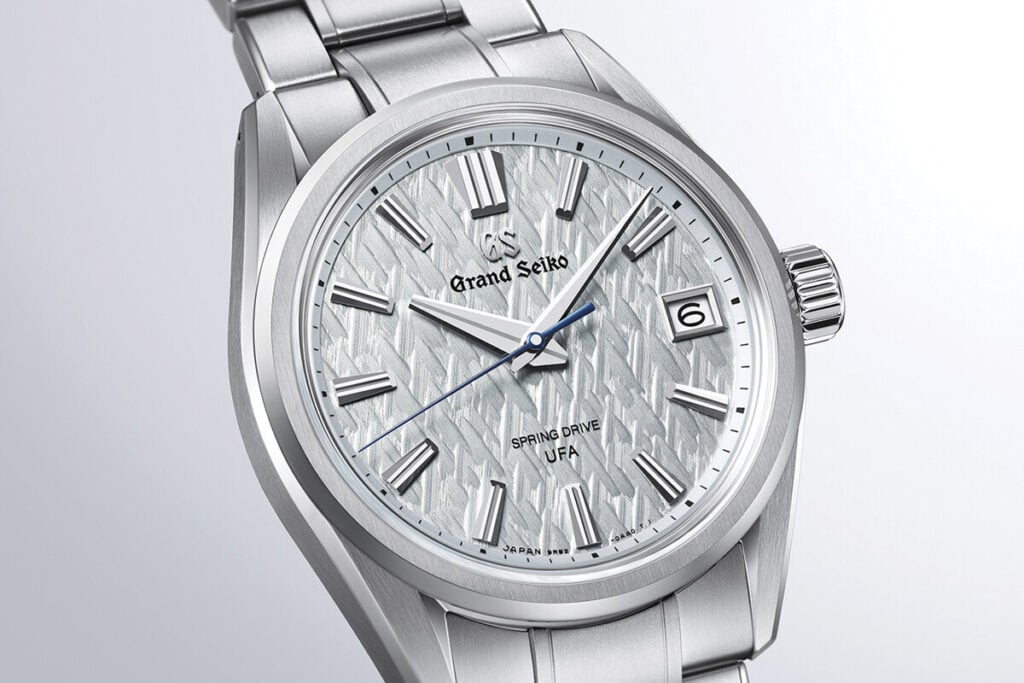 Relógio de pulso prateado com mostrador texturizado em tom claro e ponteiro dos segundos azul.