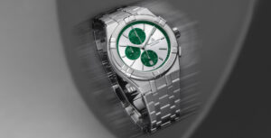 Relógio Maurice Lacroix prateado com mostrador verde e três subdials, em close-up sobre fundo desfocado.