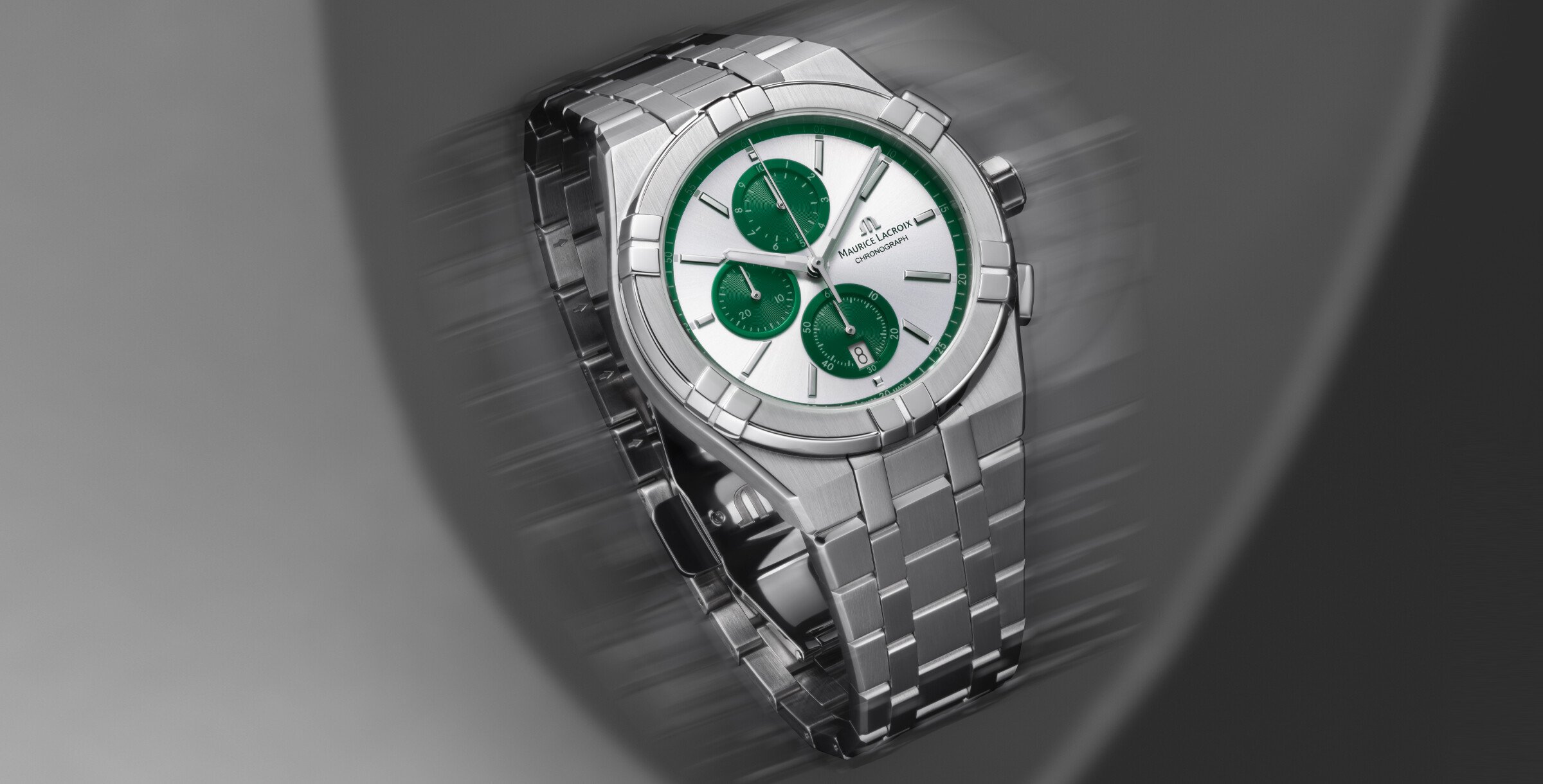Relógio Maurice Lacroix prateado com mostrador verde e três subdials, em close-up sobre fundo desfocado.