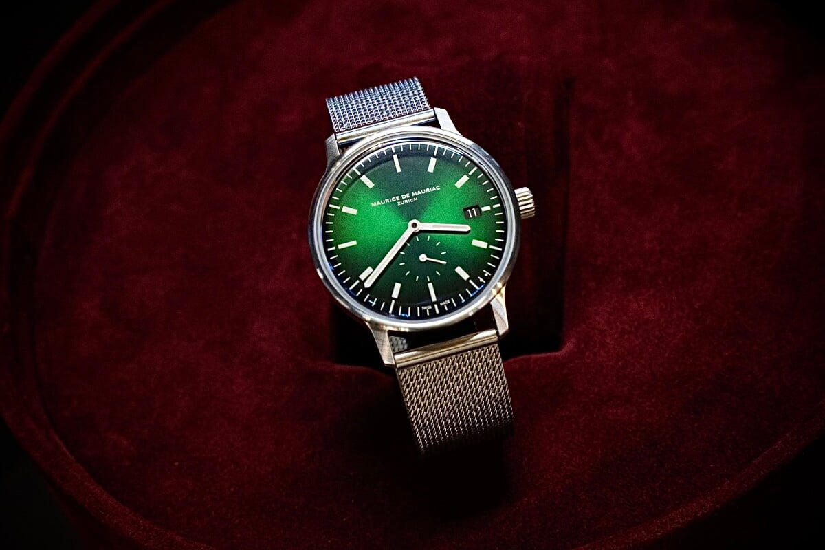 Relógio em aço com bracelete metálica e mostrador verde num expositor vermelho da marca Maurice de Mauriac, modelo L3 Small Seconds Spheric Green