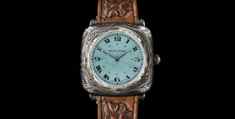 Relógio de pulso Ralph Lauren com caixa em prata e mostrador azul-turquesa. O design inclui números romanos e arábicos, com ponteiros de horas e minutos em preto. A pulseira é de couro marrom, com detalhes em relevo de folhas.