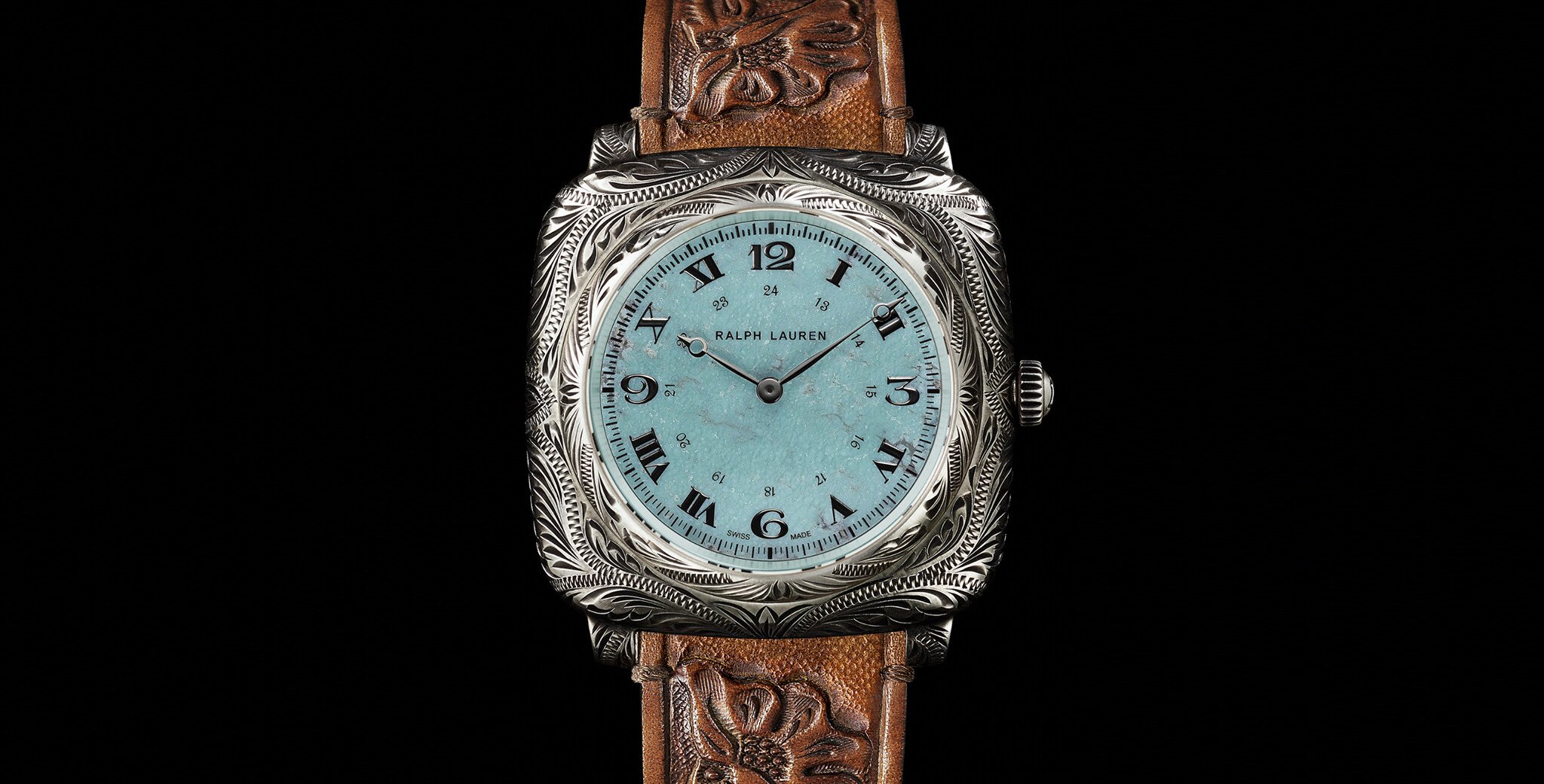 Relógio de pulso Ralph Lauren com caixa em prata e mostrador azul-turquesa. O design inclui números romanos e arábicos, com ponteiros de horas e minutos em preto. A pulseira é de couro marrom, com detalhes em relevo de folhas.