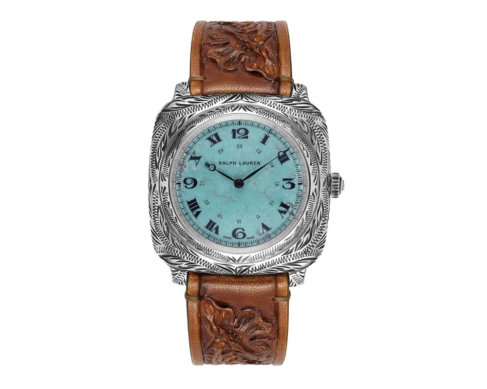 Relógio de pulso Ralph Lauren com caixa em prata e mostrador azul-turquesa. O design inclui números romanos e arábicos, com ponteiros de horas e minutos em preto. A pulseira é de couro marrom, com detalhes em relevo de folhas.