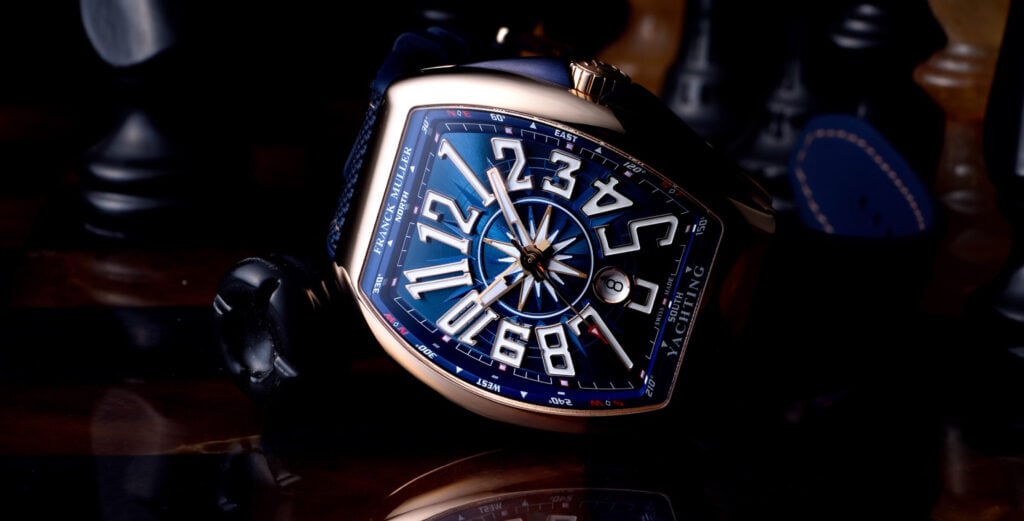Rel&oacute;gio Franck Muller Vanguard Sail Yachting, com um design sofisticado e moderno. A pe&ccedil;a exibe n&uacute;meros grandes e arredondados em um mostrador azul com detalhes em forma de b&uacute;ssola. O rel&oacute;gio est&aacute; repousado sobre um tabuleiro de xadrez, com a pe&ccedil;a de um cavalo vis&iacute;vel em primeiro plano e um fundo desfocado.