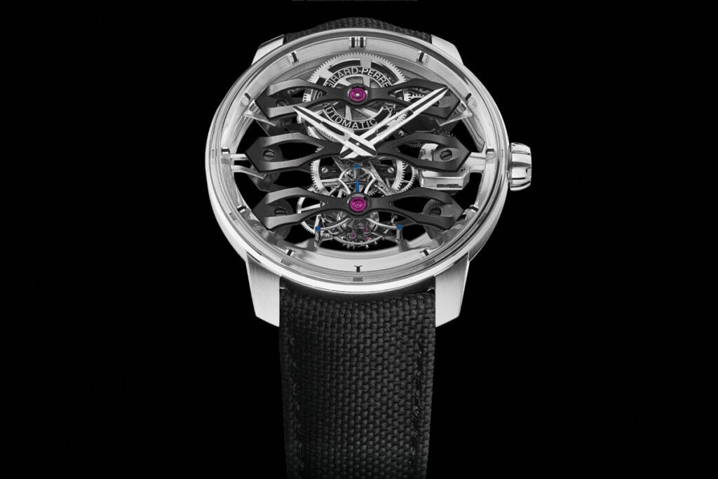 Rel&oacute;gio Girard-Perregaux com uma caixa met&aacute;lica prateada e mostrador transparente, exibindo o mecanismo interno detalhado. O design inclui tr&ecirc;s ponteiros flutuantes em metal escuro, com componentes mec&acirc;nicos vis&iacute;veis como o tourbillon e engrenagens, e rubis destacados. A pulseira &eacute; de tecido preto.