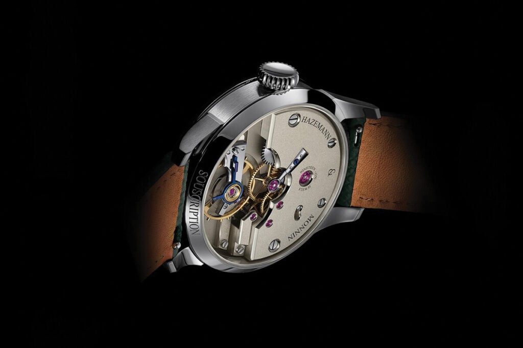 Relógio mecânico visto de lado e por trás, com o movimento exposto, caixa metálica polida e bracelete de couro castanho, sobre fundo preto.