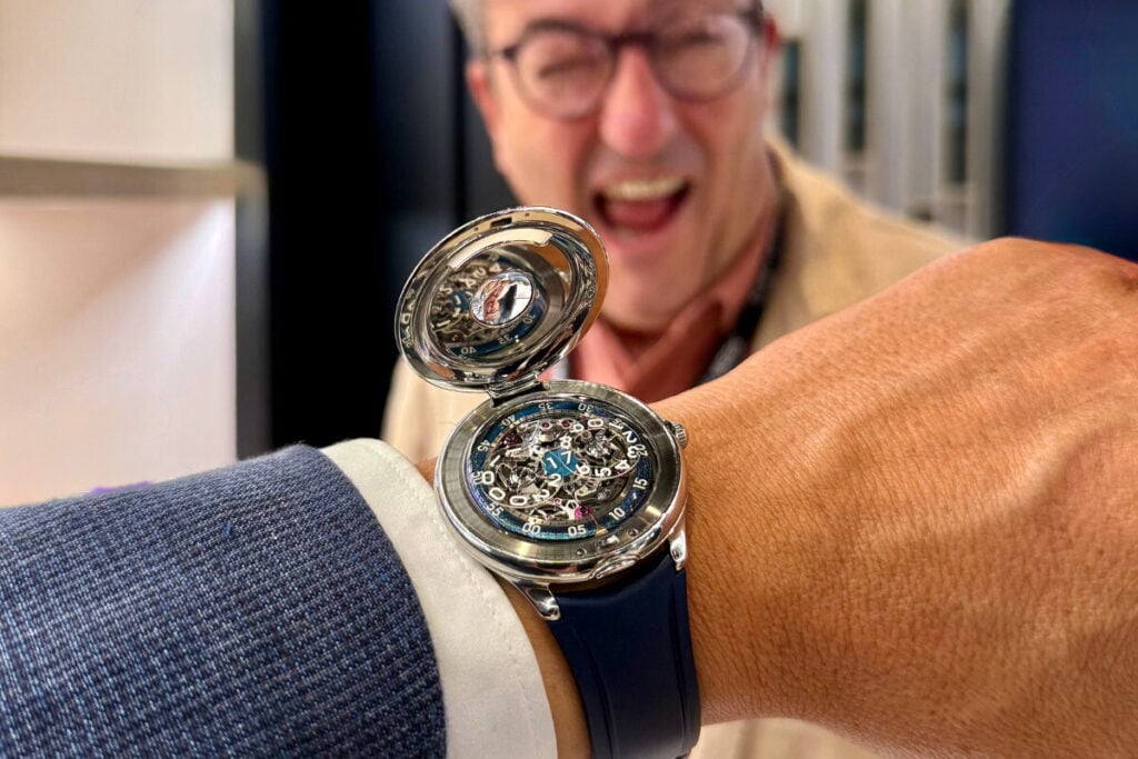 relógio no pulso com tampa aberta e discos das horas Czapek Time Jumper com homem de boca aberta por trás Xavier de Roquemaurel, CEO da Czapek