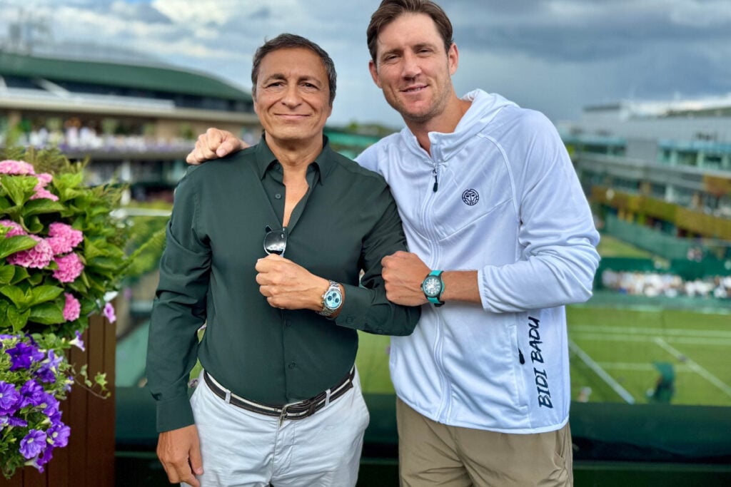 duas pessoas com rel&oacute;gios Norqain em Wimbledon com courts de t&eacute;nis de relva no fundo, Miguel Seabra com Freedom 60 Chrono e Matt Ebden com Wild One