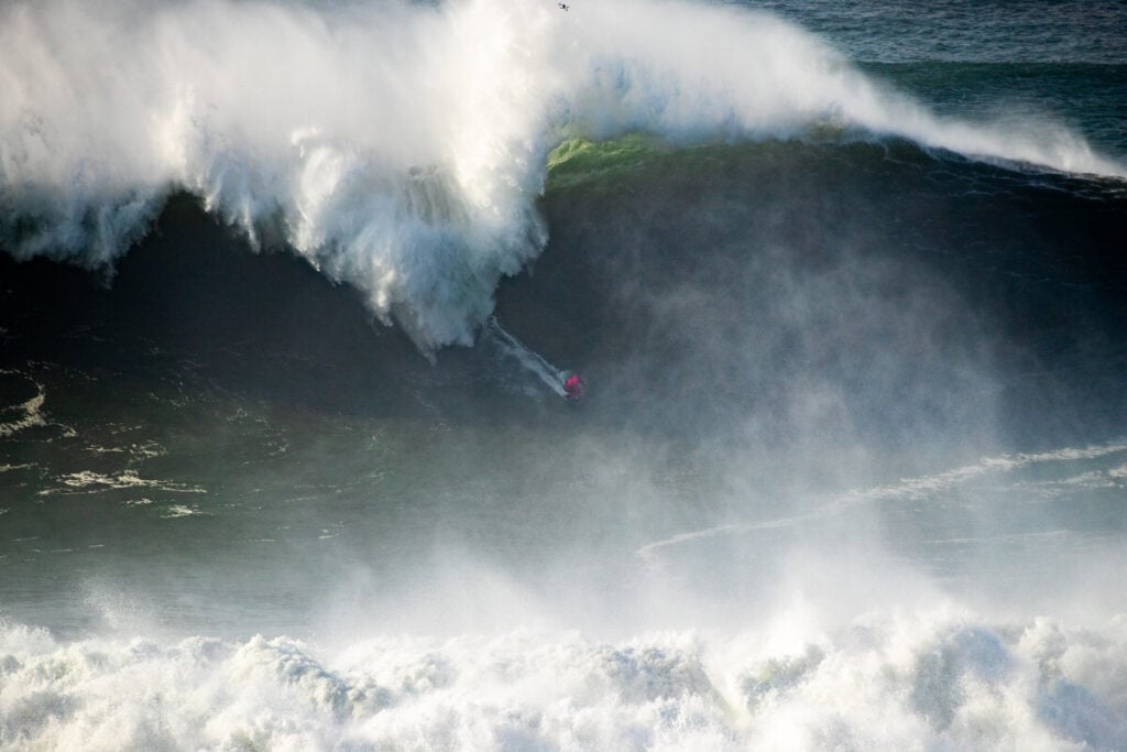 Surfista francês Clément Roseyro numa onda gigante na Nazaré, com a crista da onda a quebrar por cima