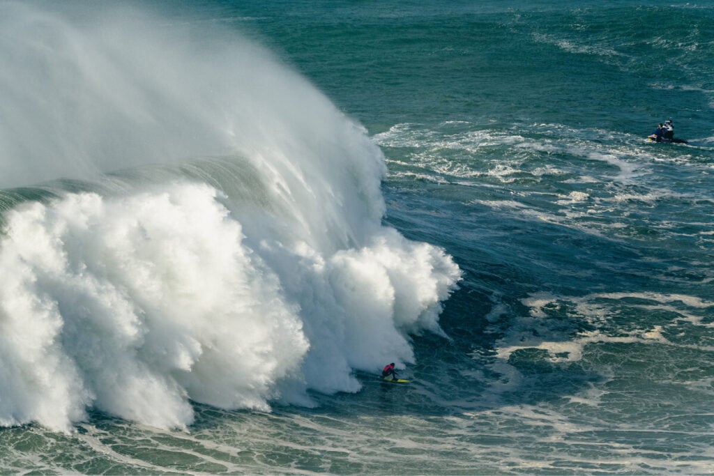 Surfista Nic Von Rupp numa onda gigante na Nazaré, com a crista da onda a quebrar por trás