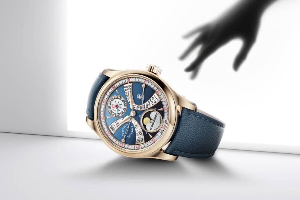 m&atilde;o que cobi&ccedil;a rel&oacute;gio de luxo Hommage La Placide da marca Roger Dubuis com mostrador azul, ponteiros em ouro retr&oacute;grados, calend&aacute;rio perp&eacute;tuo com fases da lua em aventurine e segmentos em madrep&eacute;rola