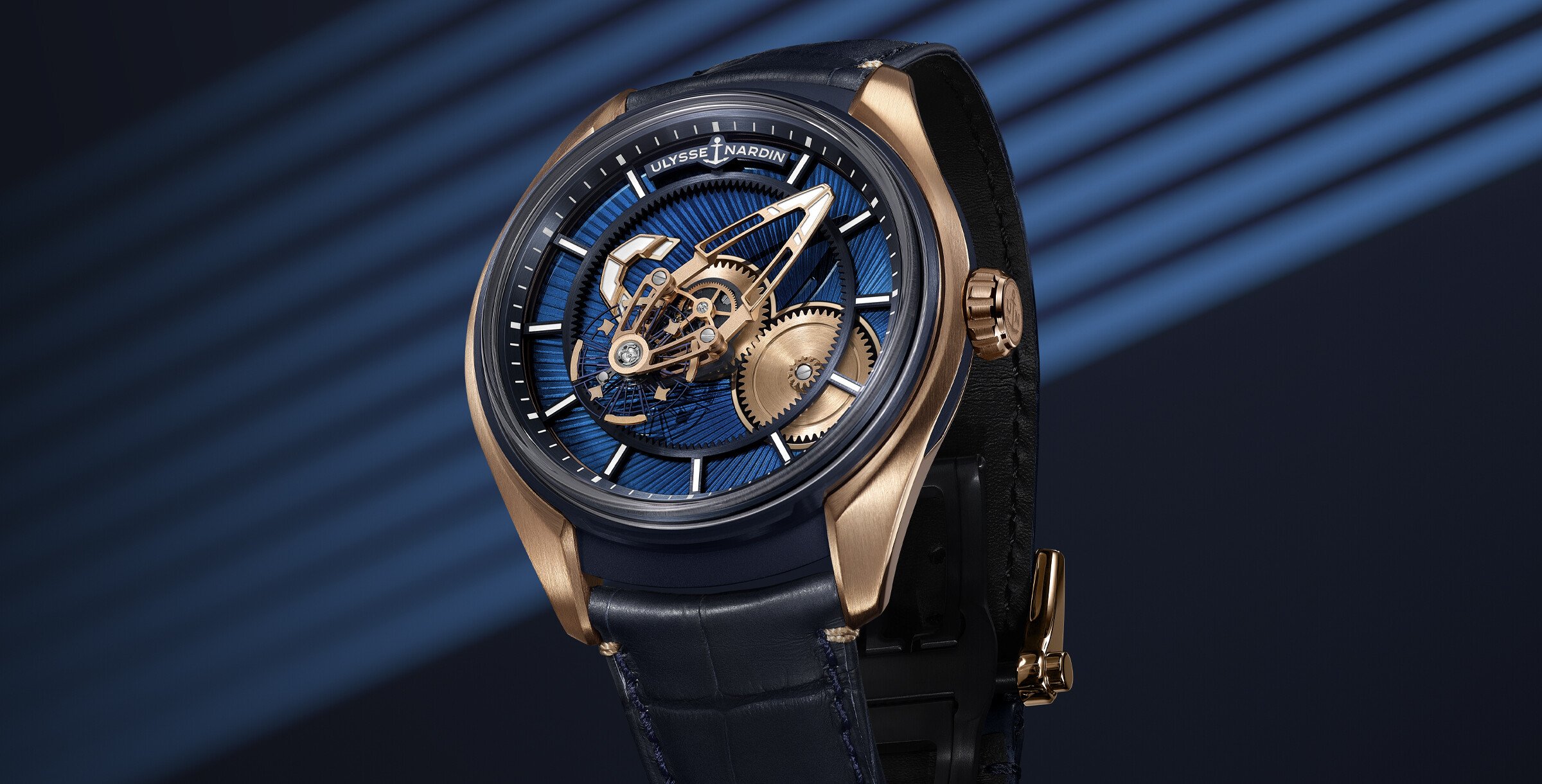 Relógio Ulysse Nardin Freak X com caixa em ouro rosa e mostrador azul. O design apresenta um movimento exposto, com engrenagens visíveis e uma combinação de elementos detalhados. O fundo azul e as linhas diagonais complementam o estilo sofisticado do relógio.