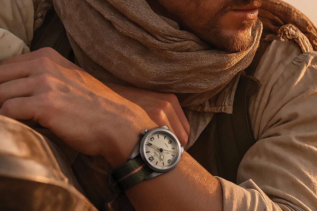 Rel&oacute;gio de pulso com mostrador claro e bracelete em tecido no bra&ccedil;o de uma pessoa vestida com roupa de deserto.