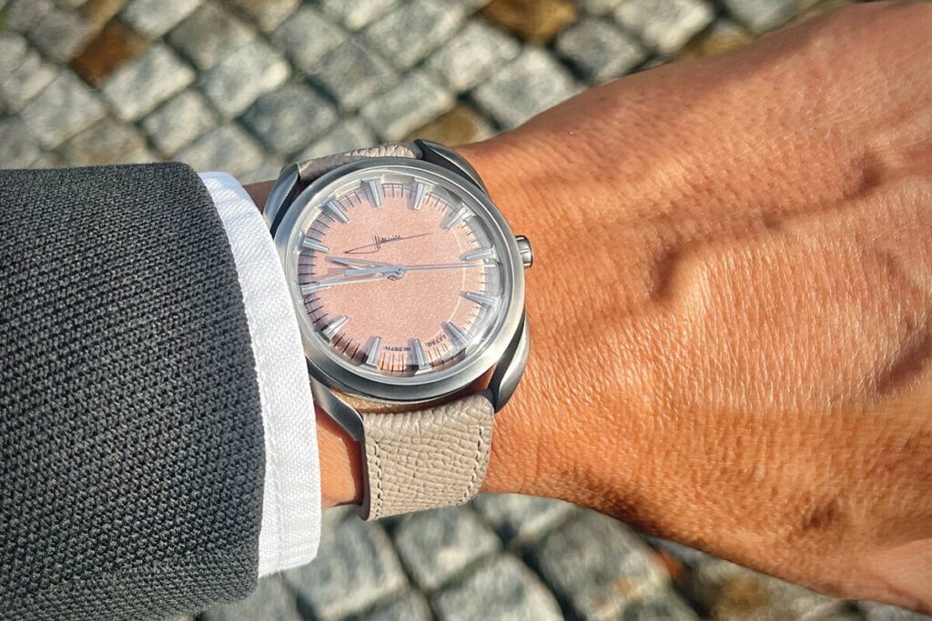 Rel&oacute;gio Holthinrichs com mostrador ros&eacute; e pulseira de couro claro, usado no pulso de uma pessoa, fotografado ao ar livre sobre piso de pedras.