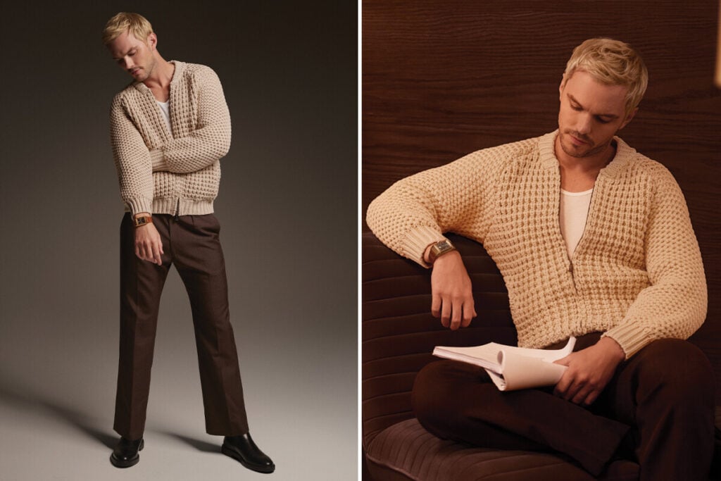 Homem loiro em ambiente de est&uacute;dio, usando um casaco de malha bege, cal&ccedil;as castanhas e um rel&oacute;gio no pulso.