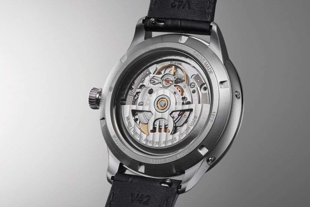 Imagem do verso de um rel&oacute;gio de luxo Maurice Lacroix, mostrando a complexidade dos mecanismos internos. O movimento &eacute; vis&iacute;vel atrav&eacute;s da parte traseira da caixa, destacando os componentes de a&ccedil;o inoxid&aacute;vel e as engrenagens. A pulseira &eacute; de couro preto e o design &eacute; refinado e t&eacute;cnico.