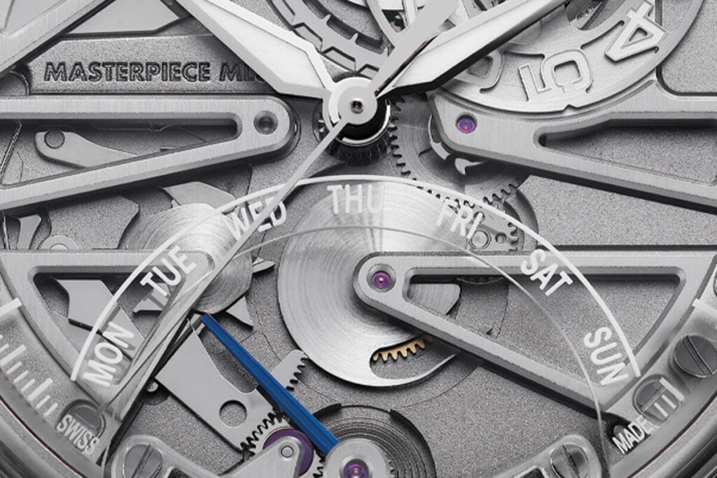 Imagem detalhada do mostrador esquel&eacute;tico de um rel&oacute;gio Maurice Lacroix, com destaque para o mecanismo interno e os dias da semana (segunda-feira a domingo) vis&iacute;veis em uma curva. O movimento das engrenagens, com detalhes met&aacute;licos e roxos, &eacute; evidenciado, juntamente com a marca "MASTERPIECE" e a inscri&ccedil;&atilde;o "SWISS" na parte inferior do mostrador.