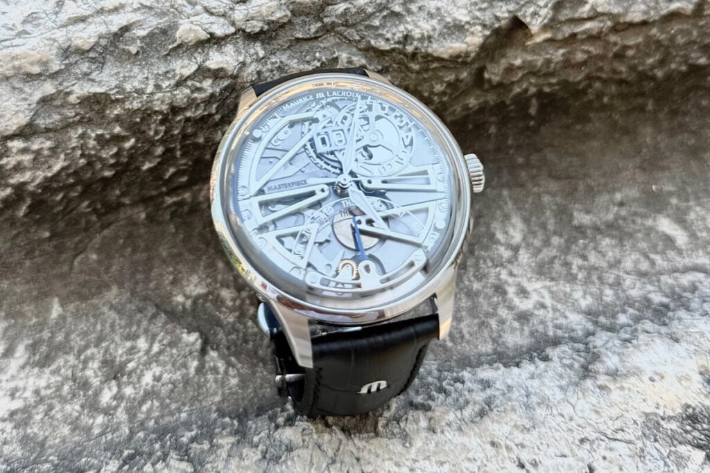 Rel&oacute;gio Maurice Lacroix com mostrador esquel&eacute;tico em primeiro plano, posicionado sobre uma superf&iacute;cie rochosa. O design detalhado das engrenagens &eacute; vis&iacute;vel, assim como o n&uacute;mero 08 na data e os dias da semana. O rel&oacute;gio possui caixa de a&ccedil;o inoxid&aacute;vel e uma pulseira de couro preto, com o logotipo da marca gravado na fivela.